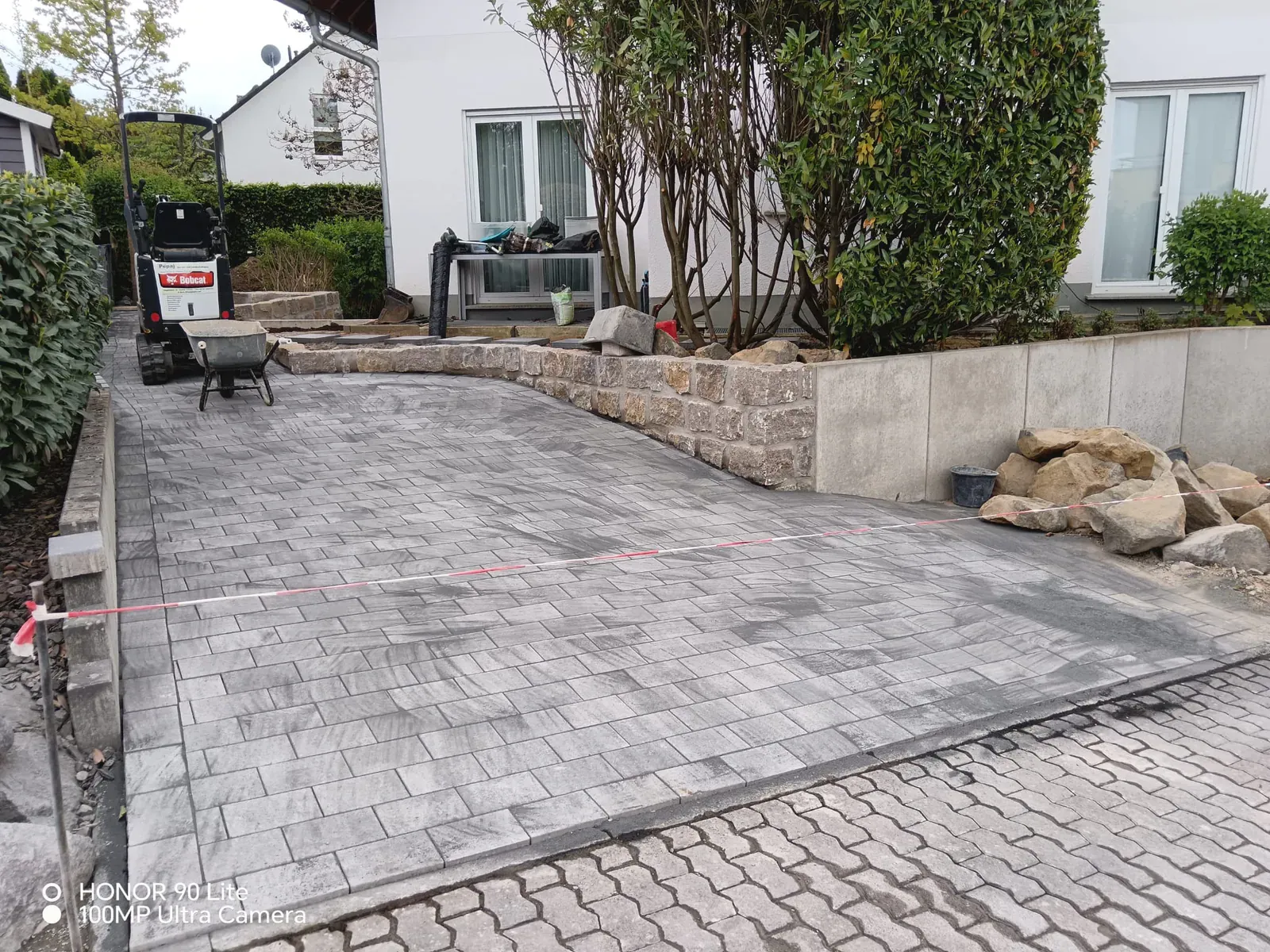 Neu gepflasterte Hoffläche mit Gefälleausbildung, Linienentwässerung und Natursteinanschlüssen.