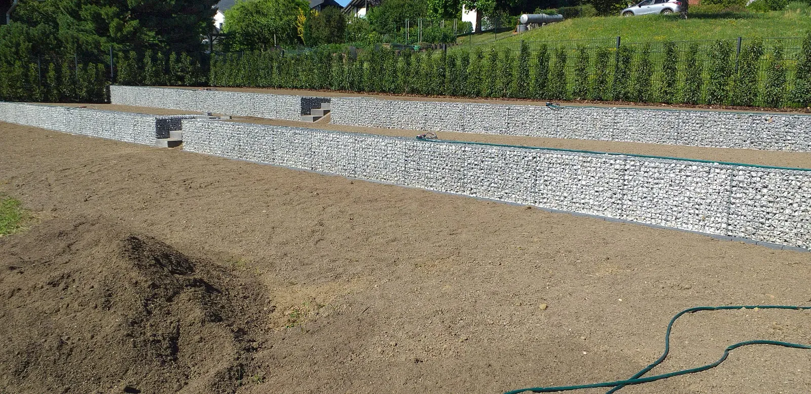 Mehrstufige Hangabfangung aus steingefüllten Gabionen mit mittig integrierter Treppenanlage.
