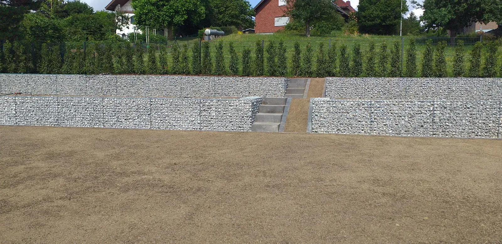 Panorama einer großflächigen Geländeterrassierung mit Gabionen, Treppe und vorbereitetem Oberboden.
