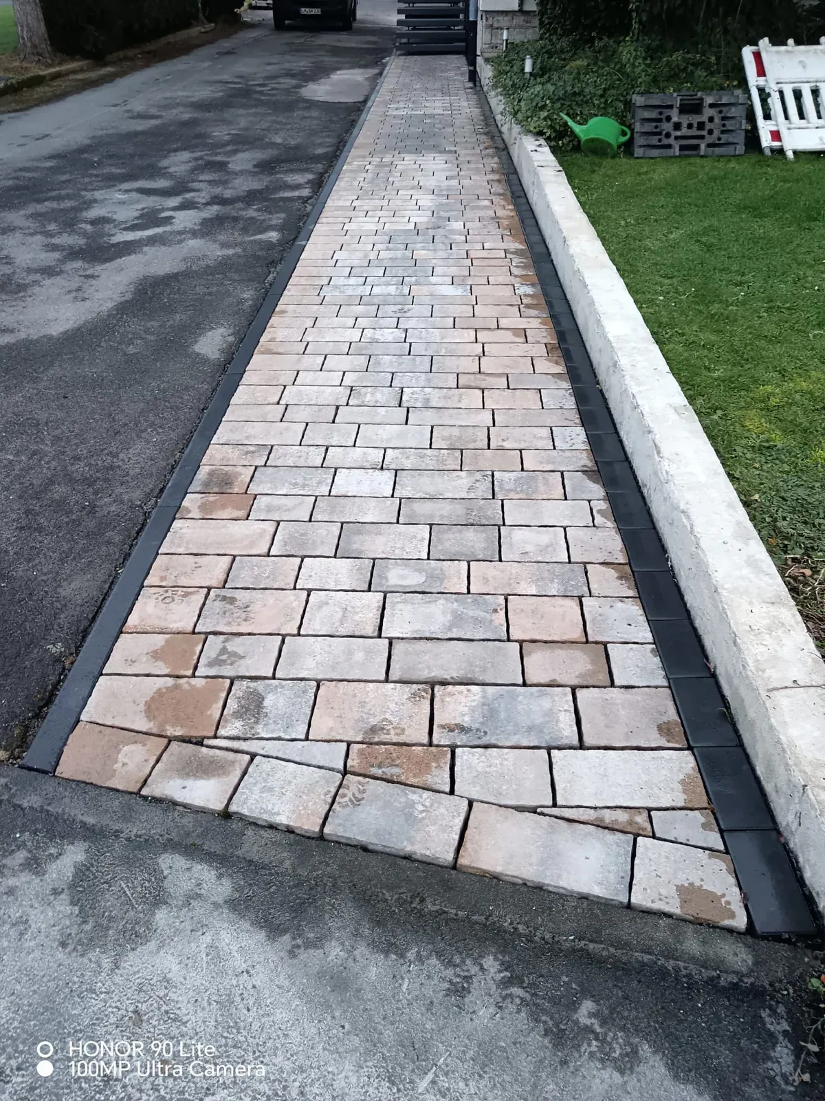 Geradliniger Pflasterweg entlang einer Rasenfläche mit kontrastierender anthrazitfarbener Kante.