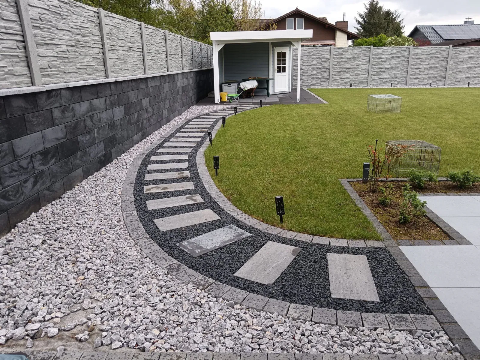 Dynamisch geführter Weg mit hellem Flächenpflaster, dunklen Querbändern und präziser Randeinfassung.