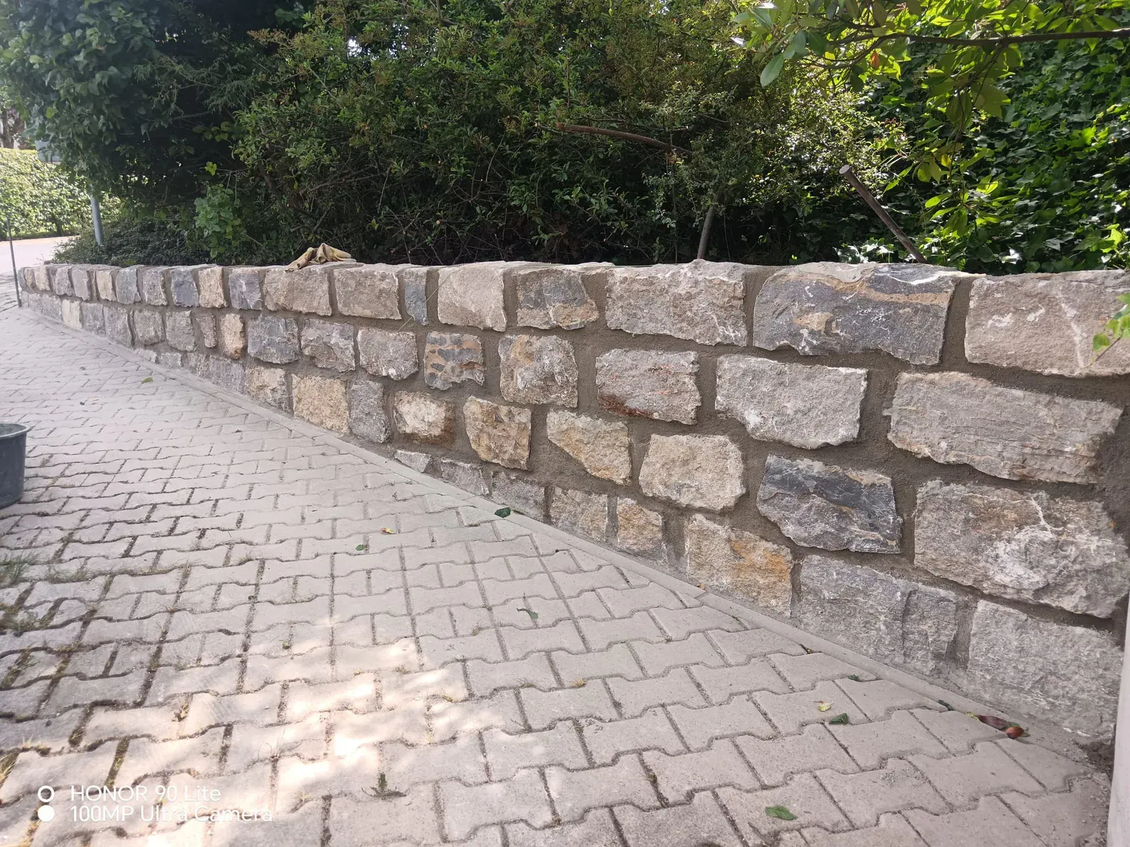 Geradlinige Stützmauer aus großformatigen Granitsteinen als robuste Einfassung einer gepflasterten Zufahrt.
