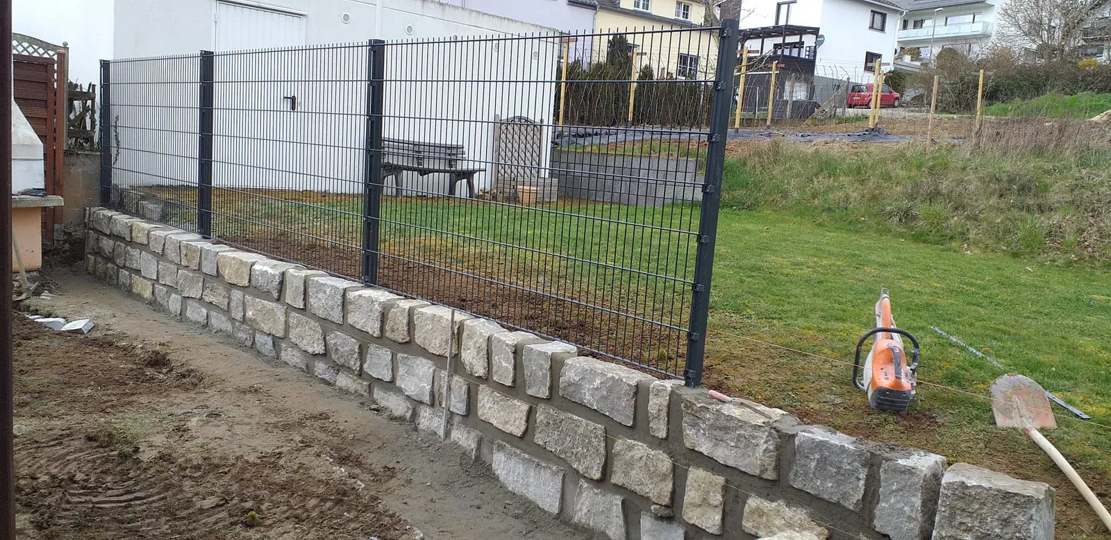 Schwarzer Doppelstabmattenzaun auf einer stabilen Sockelmauer aus hellem Naturstein.