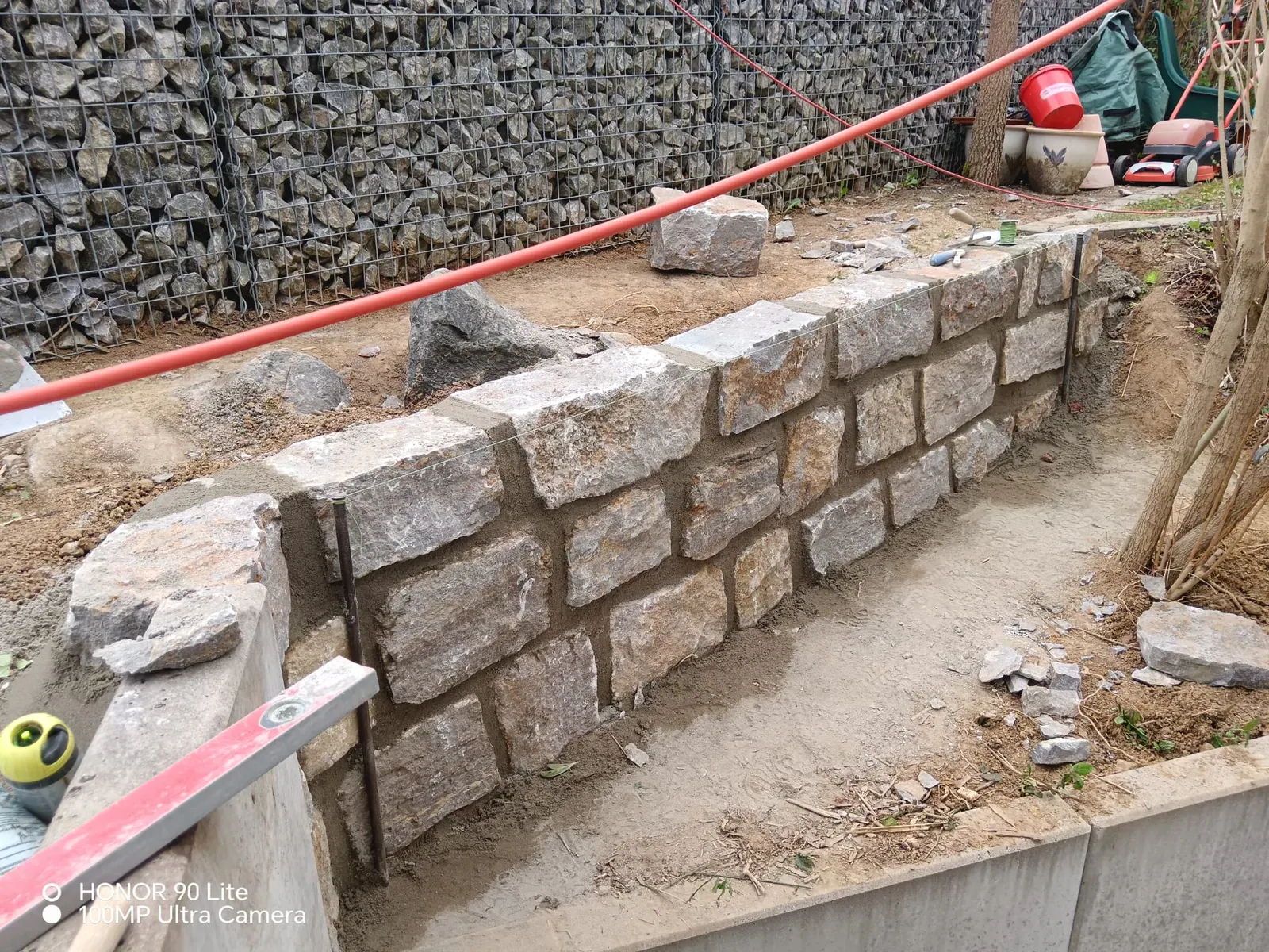 Handwerkliche Bauphase einer massiven Mauer aus behauenen Natursteinen mit ausgerichteter Schnurführung.