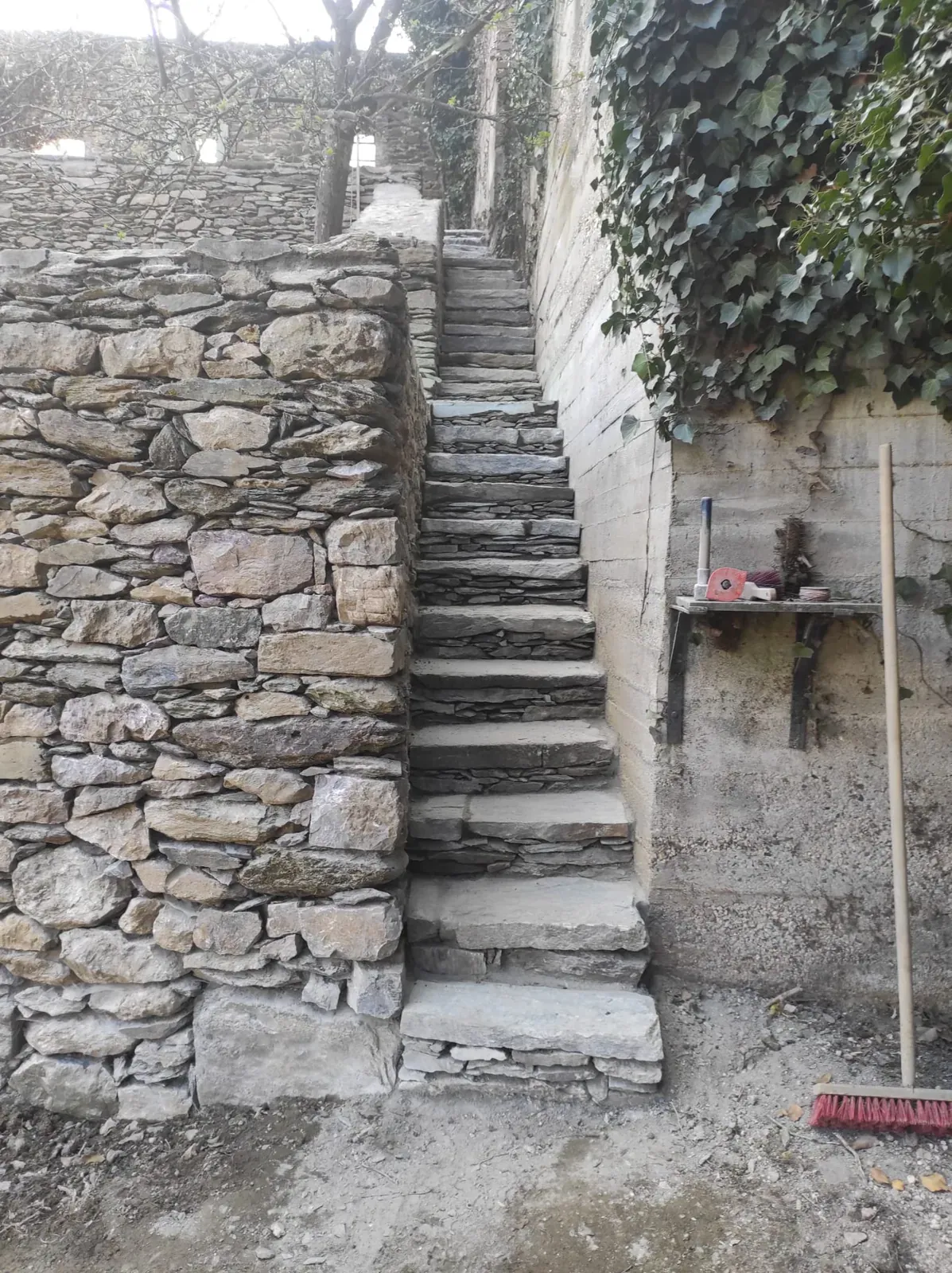 Traditionell wirkende Natursteinarbeit mit schmaler Treppe und tragender Mauer in anspruchsvollem Gelände.