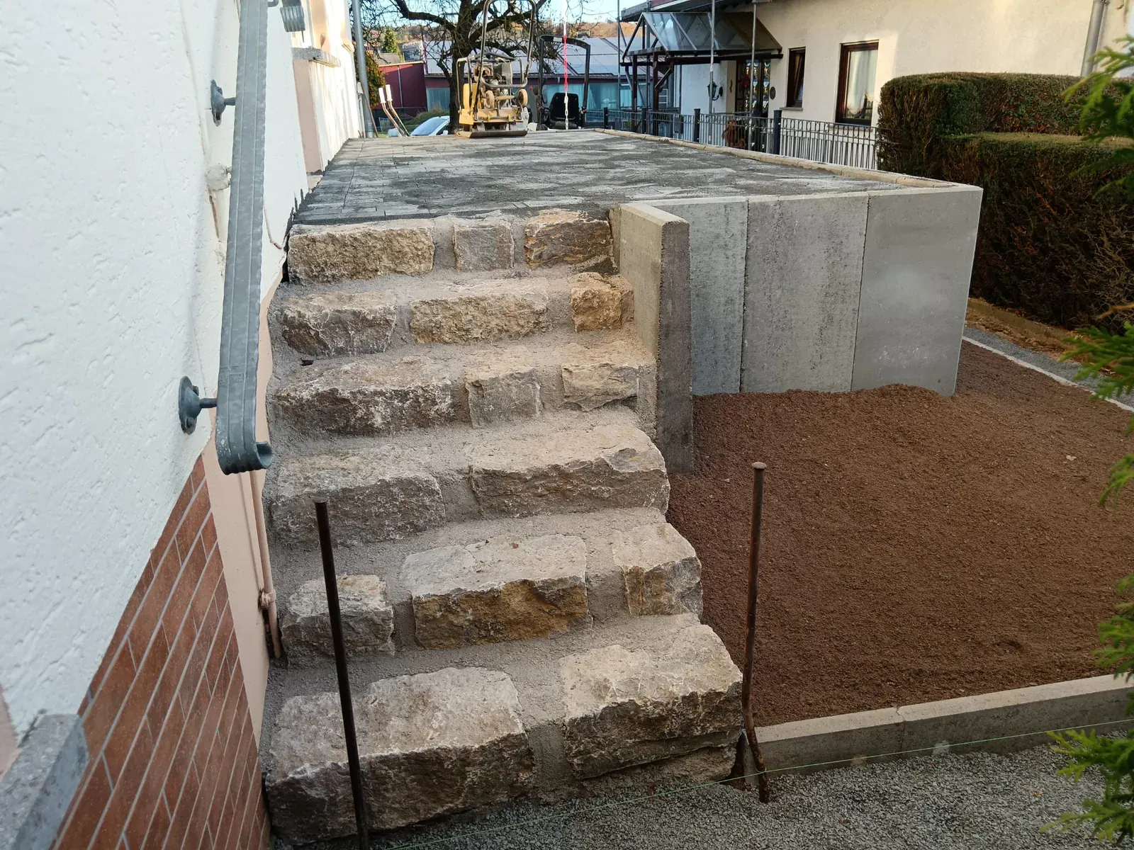 Neu gesetzte Außentreppe aus Naturstein zwischen verputztem Haus und massiven seitlichen Stützwänden.