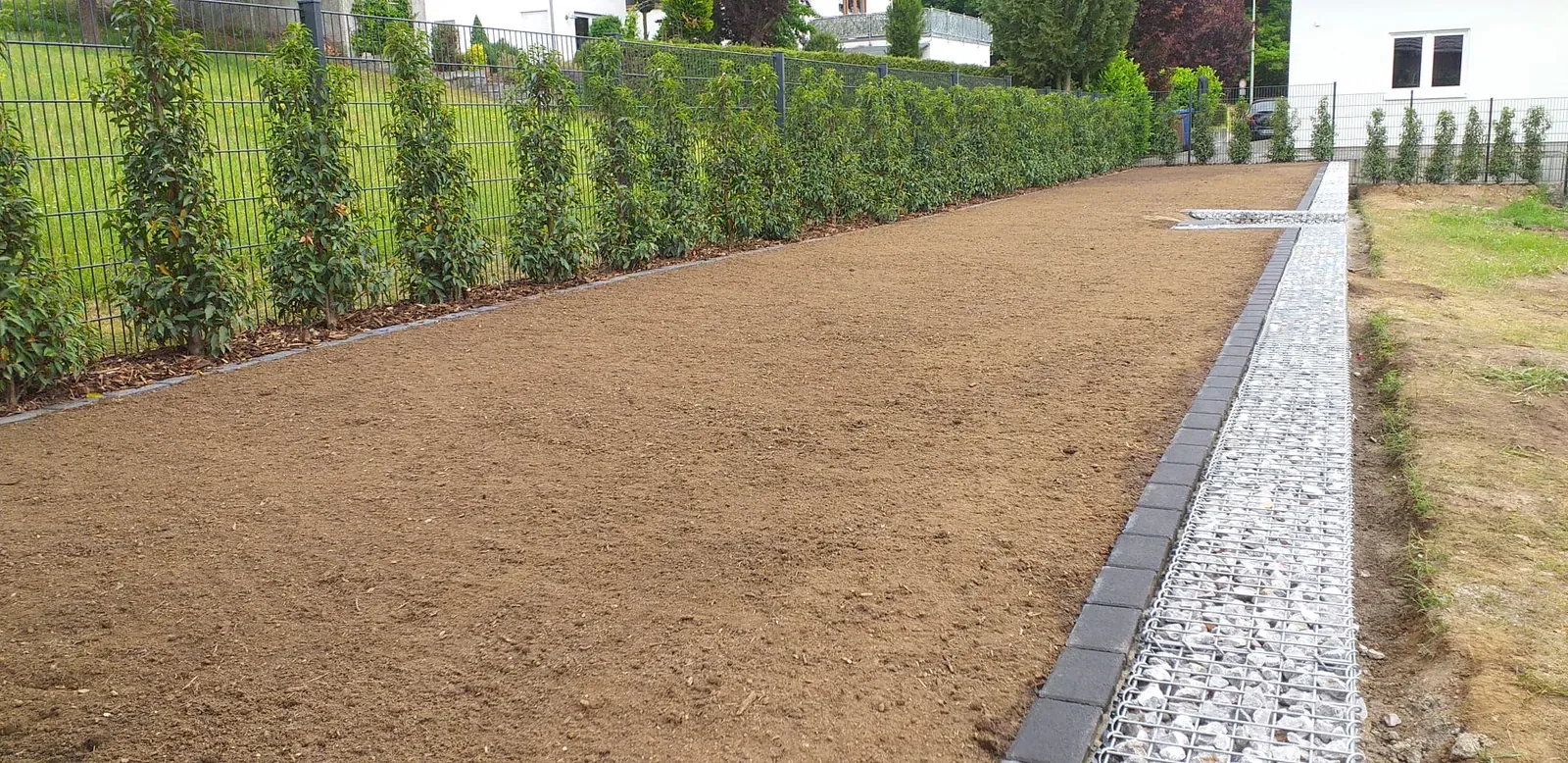 Sorgfältig abgezogene Bodenfläche mit gerader Pflasterkante als Vorbereitung für eine neue Rasenanlage.
