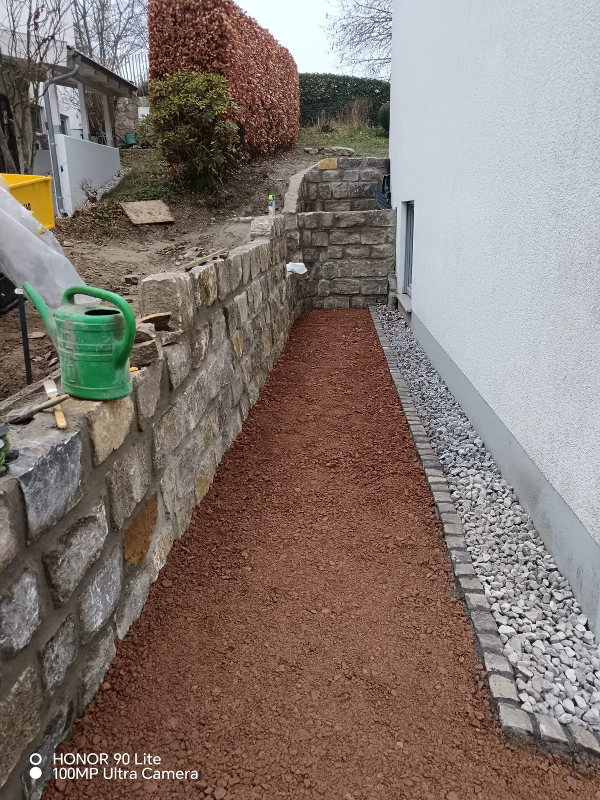 Massive Stützmauer entlang des Gebäudes mit mineralischer Drainage- und Mulchfläche.
