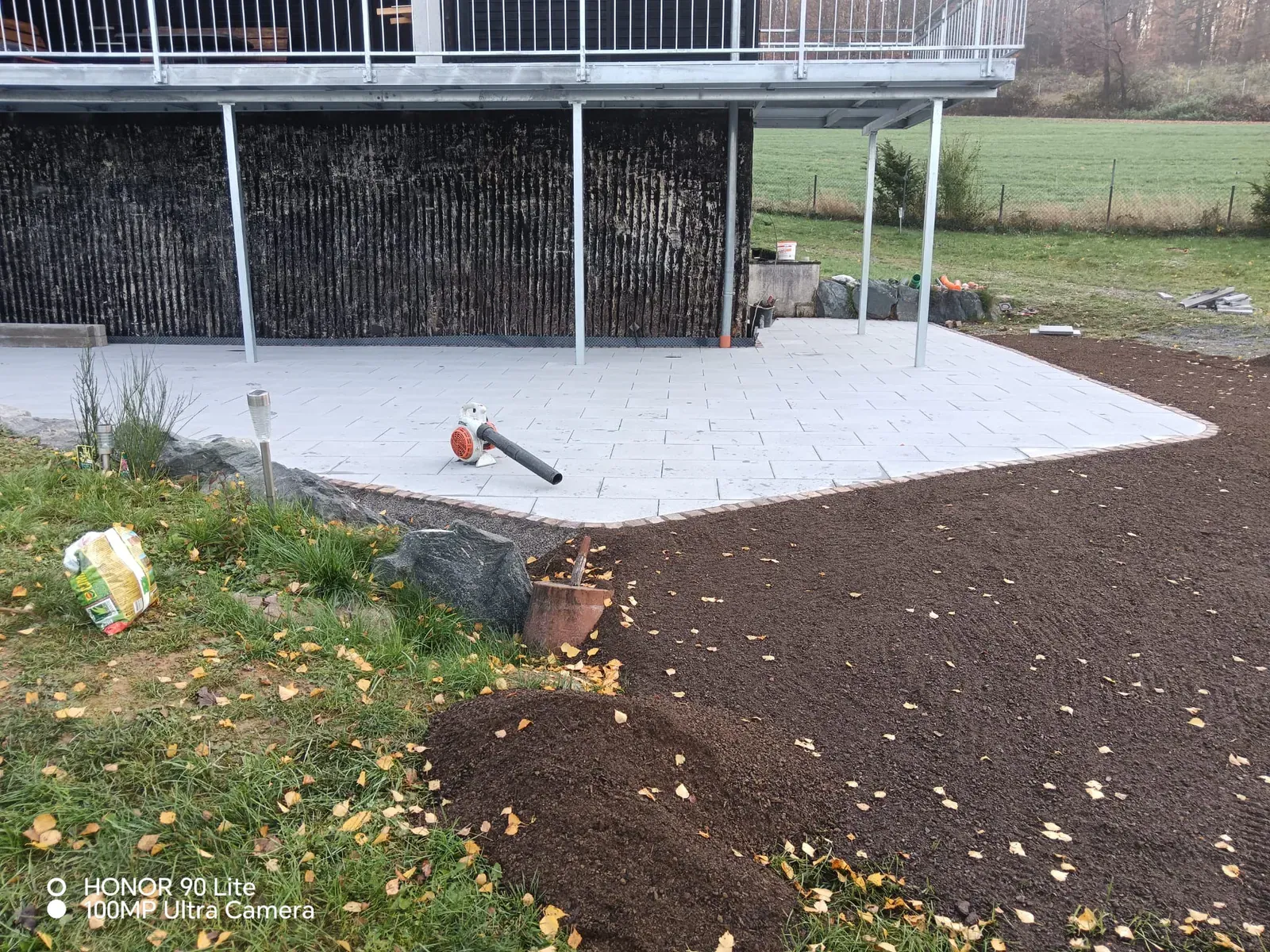 Neu belegte Terrasse am Haus mit vorbereiteten Pflanz- und Rasenflächen.