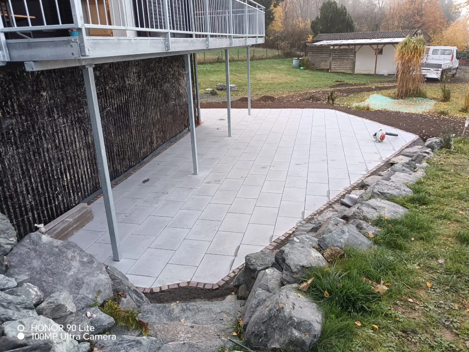 Großzügige Terrassenfläche unter dem Balkon mit gleichmäßig verlegten grauen Platten und sauberer Randführung.