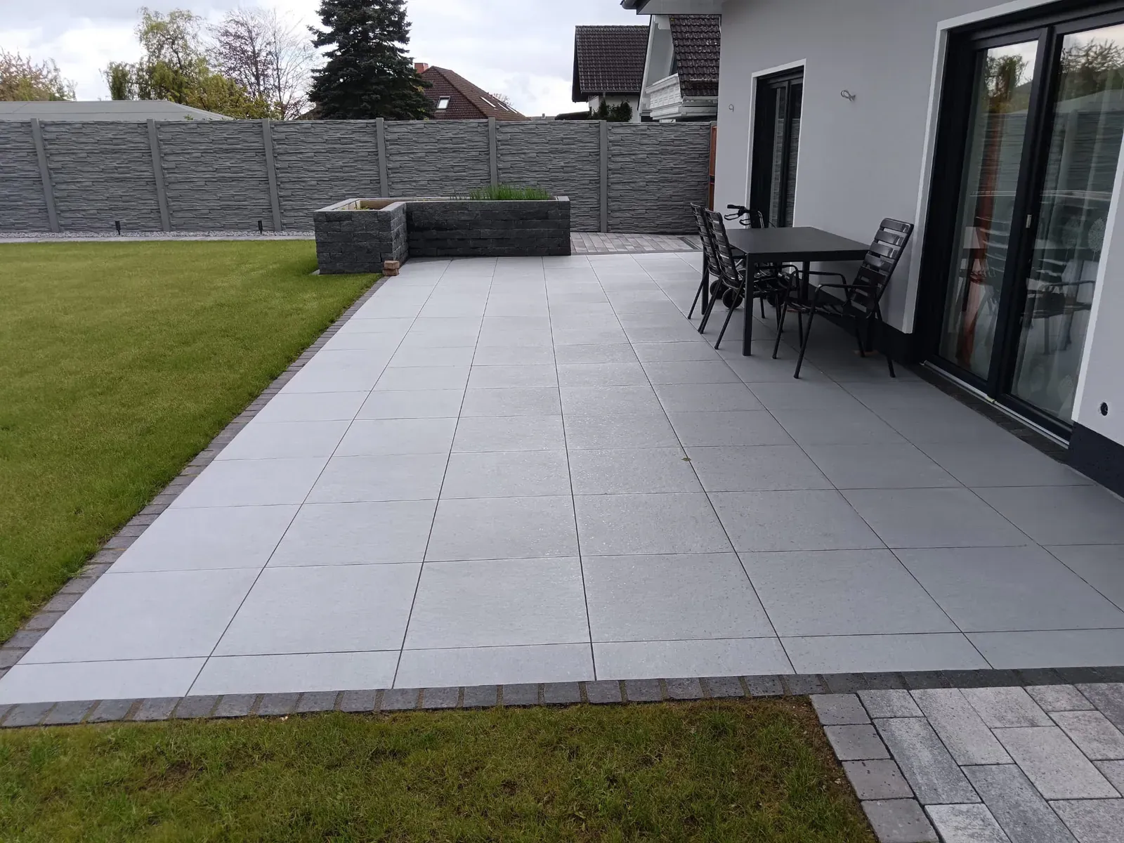 Fertige Terrassenfläche am Wohnhaus mit ruhigem Fugenbild, Sitzbereich und weitem Rasenblick.