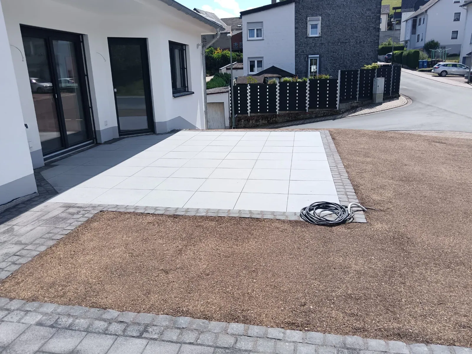 Helle, großformatige Terrassenplatten am modernen Wohnhaus mit vorbereiteter Gartenfläche.