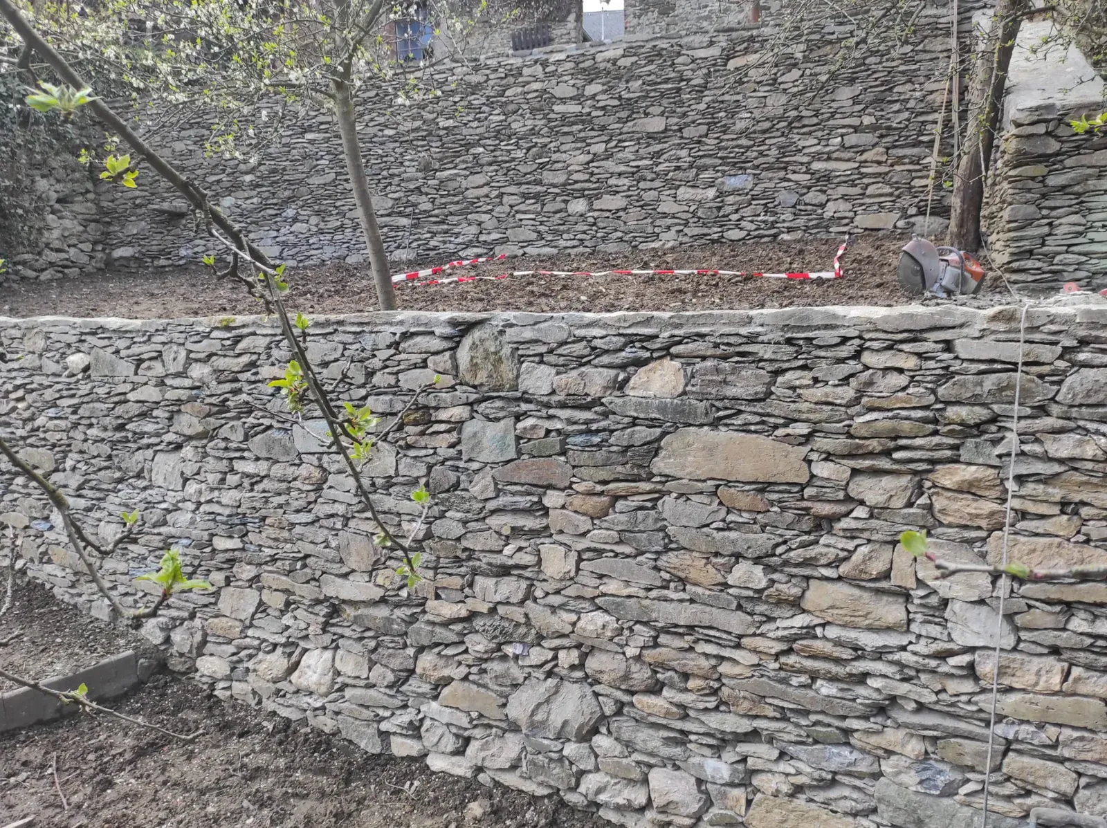 Handgesetzte Trockenmauer aus unregelmäßigen Natursteinen entlang eines bepflanzten Hangs.