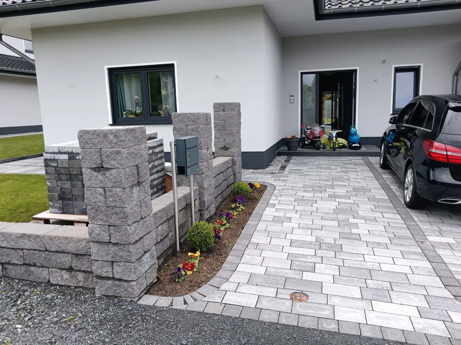 Gestalteter Hauseingang mit mehrfarbigem Pflaster, gemauerten Säulen und bepflanzter Randeinfassung.