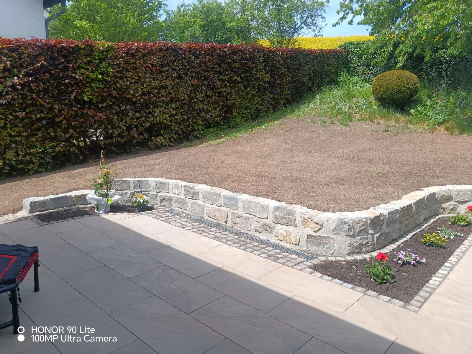 Neu modellierter Vorgarten mit geschwungener Natursteinmauer, kleinen Pflanzinseln und vorbereitetem Rasenplanum.