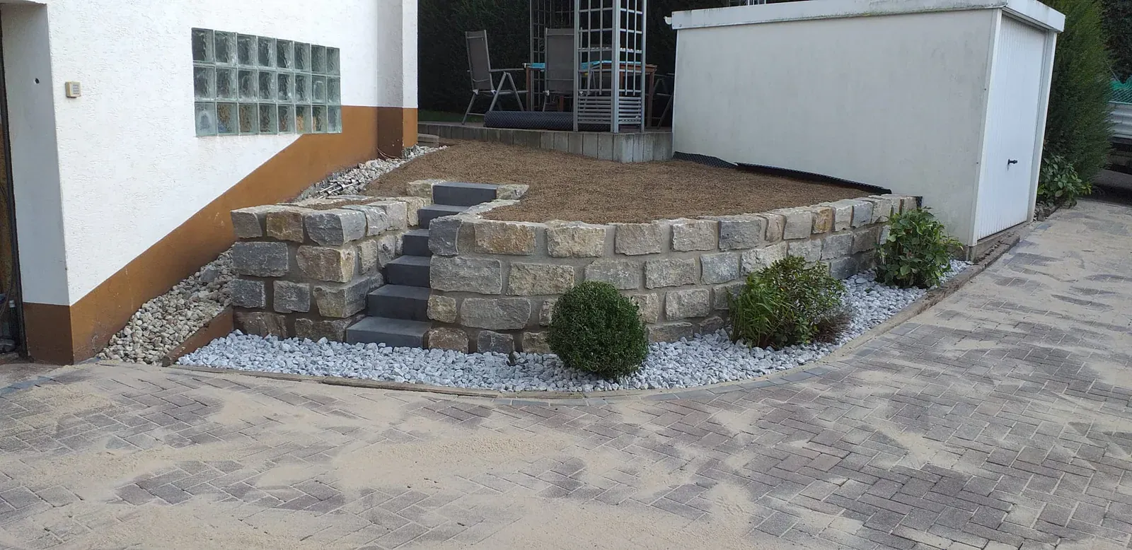 Neu gestalteter Hauseingang mit massiven Natursteinstufen, Trockenmauer und kontrastierendem Ziersplitt.